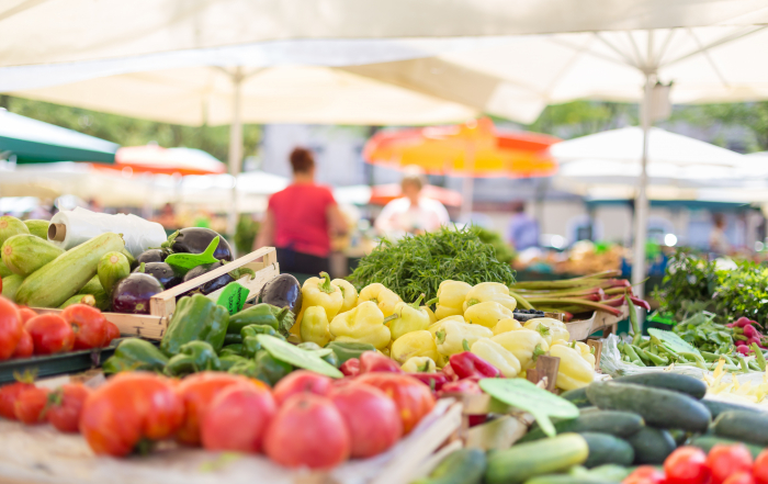 Farmers' food market stall with variety of organic vegetable. Vendor serving and chating with customers.